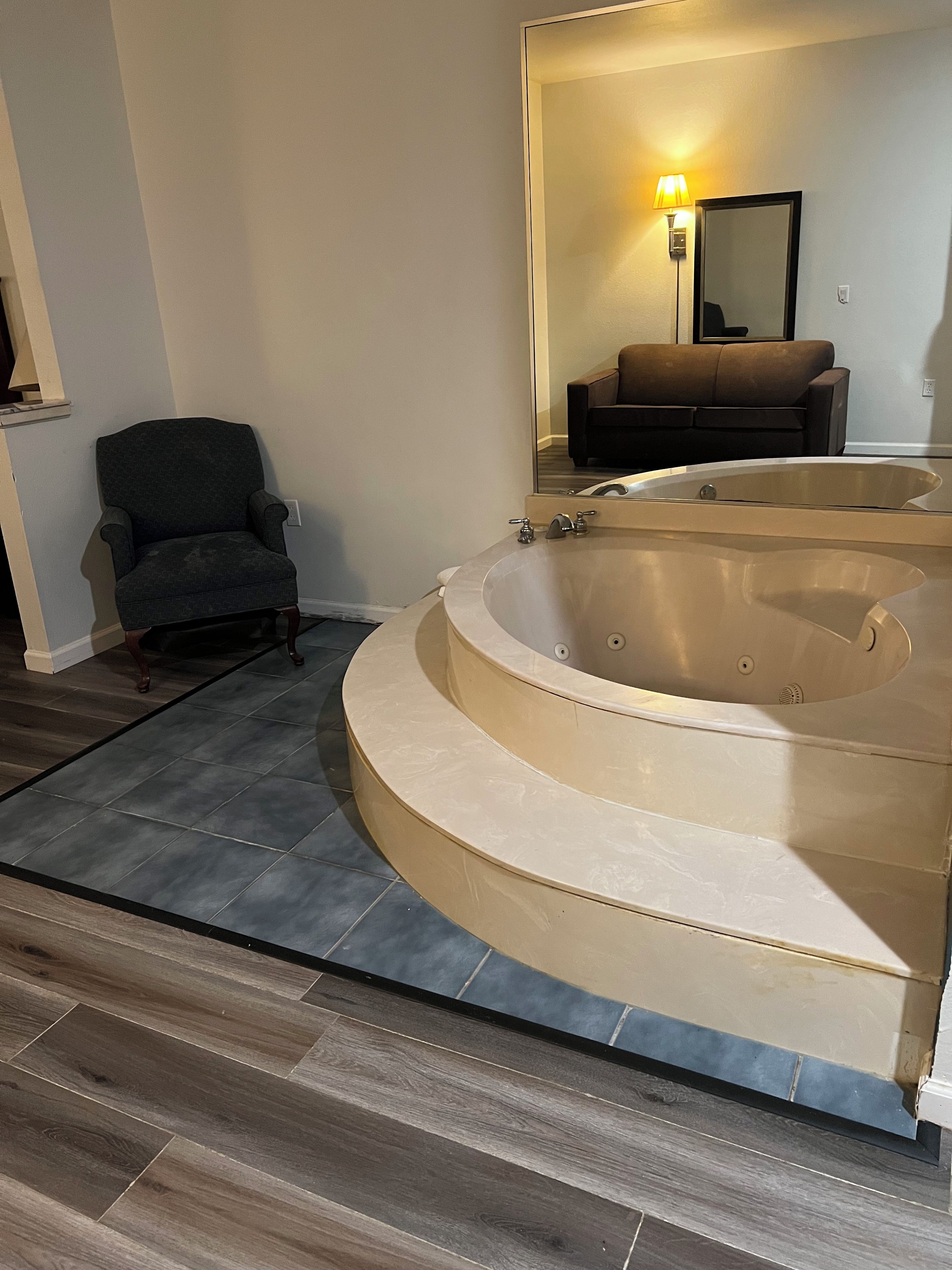 A bathroom with a large bathtub, a chair, and a sofa in the background.