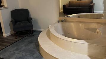 A bathroom with a large bathtub, a chair, and a sofa in the background.