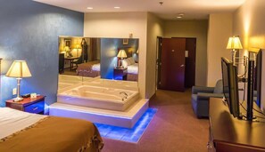 A hotel room with a large bed, a separate sitting area, a bathtub, and a mirror reflecting the room.