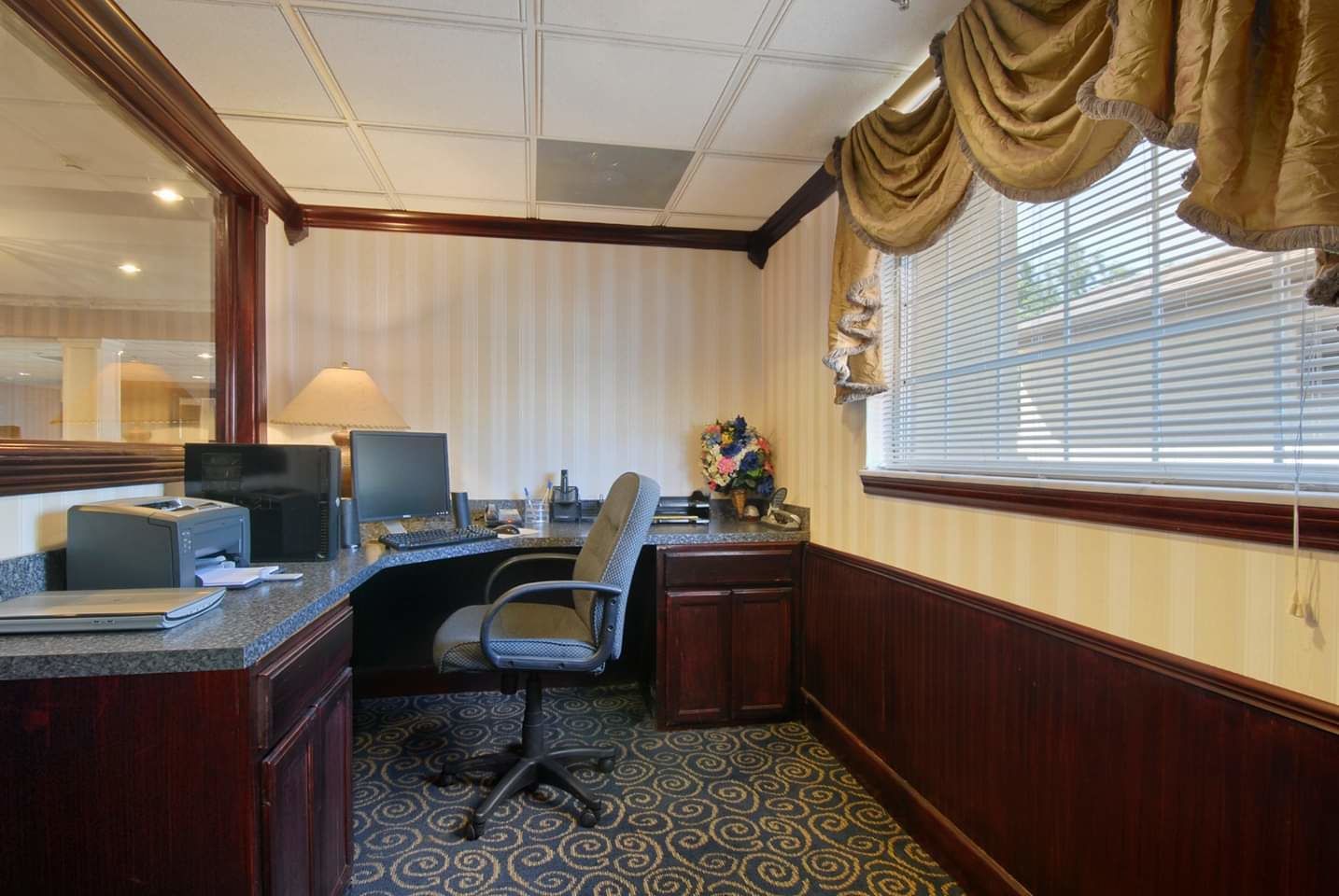 A hotel office with a desk, computer, printer, and a chair.