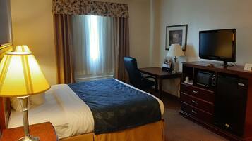 Una habitación de hotel con cama, escritorio, televisión y ventana con cortinas.