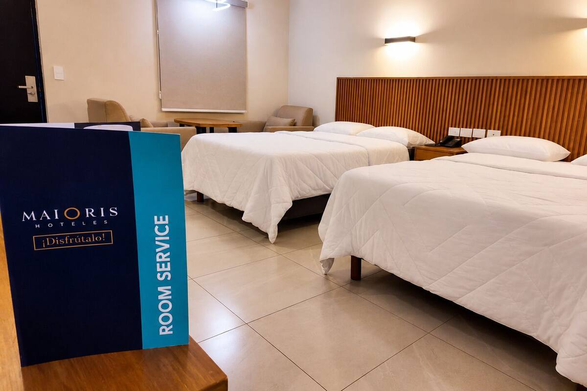 Une chambre d’hôtel avec deux lits, une tête de lit en bois, une table de chevet avec un téléphone et une lampe fixée au mur.