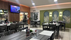 Een restaurant met meerdere tafels en stoelen, een televisiescherm en een receptiehoek.