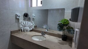 Ein Badezimmer mit Waschbecken, Handtuchhalter, Händetrockner und einer Topfpflanze.