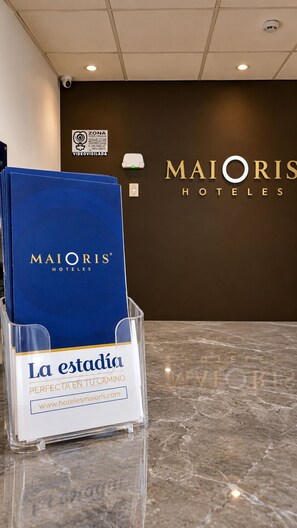 Rezeption des Hotels MAJORIS mit einem blauen Broschürenständer des Hotels MAJORIS und einem Schild mit der Aufschrift 'La estación PERFECTA EN TU CAMINO'.