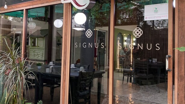 Een restaurant met een bord waarop 'Restaurant' staat, een glazen deur en een betegeld terras met tafels en stoelen.