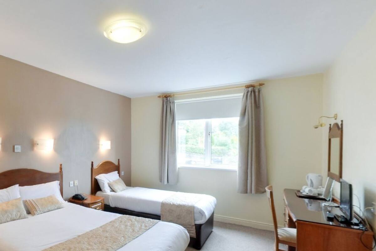 Habitación de hotel con dos camas, un escritorio y una ventana con cortinas.