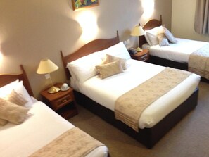 A hotel room with three single beds, each with a wooden headboard, bedside tables with lamps, and a beige carpet. - Hotel Curracloe (Curracloe)