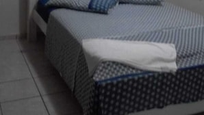 A bedroom with a bed, white walls, and an air conditioning unit above the bed. - Apartamento Ponta Negra (Natal)