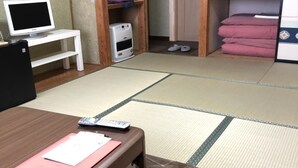 Una habitación con suelo de tatami, un escritorio de madera con una computadora y papeles, un calentador pequeño y una cama individual con ropa de cama rosa.