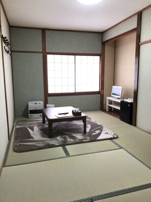 A traditional Japanese room with tatami flooring, a low table with a cushion, a heater, a TV on a stand, and a sliding door. - Oyado Zen (Kusatsu)