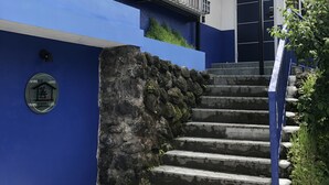 Un edificio con fachada azul y blanca, un muro de piedra y un conjunto de escaleras de concreto que llevan a una puerta.