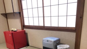 Una habitación con esteras de tatami, un calentador rojo, un aire acondicionado gris y un bote de basura blanco.