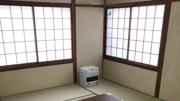 Una habitación con estera de tatami, futón, un calentador pequeño y ventana con diseño de cuadrícula.
