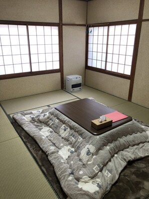 A tatami mat room with a futon bed, a small heater, and a window with a grid pattern. - Oyado Zen (Kusatsu)