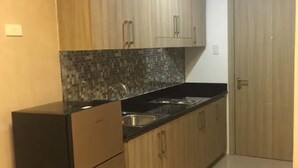 A compact kitchen with wooden cabinets, a black refrigerator, and a tiled backsplash.