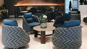 A modern lobby with grey woven armchairs, a central round table with a vase, and a contemporary reception desk.
