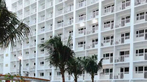 A modern hotel with a large indoor swimming pool, surrounded by lush greenery and palm trees.