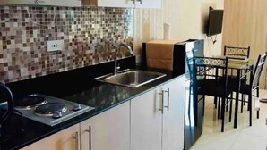 A modern kitchen with a black countertop, stainless steel sink, and white cabinets. There is a dining area with a table and chairs. - Breeze Residences by Ridged (Pasay)