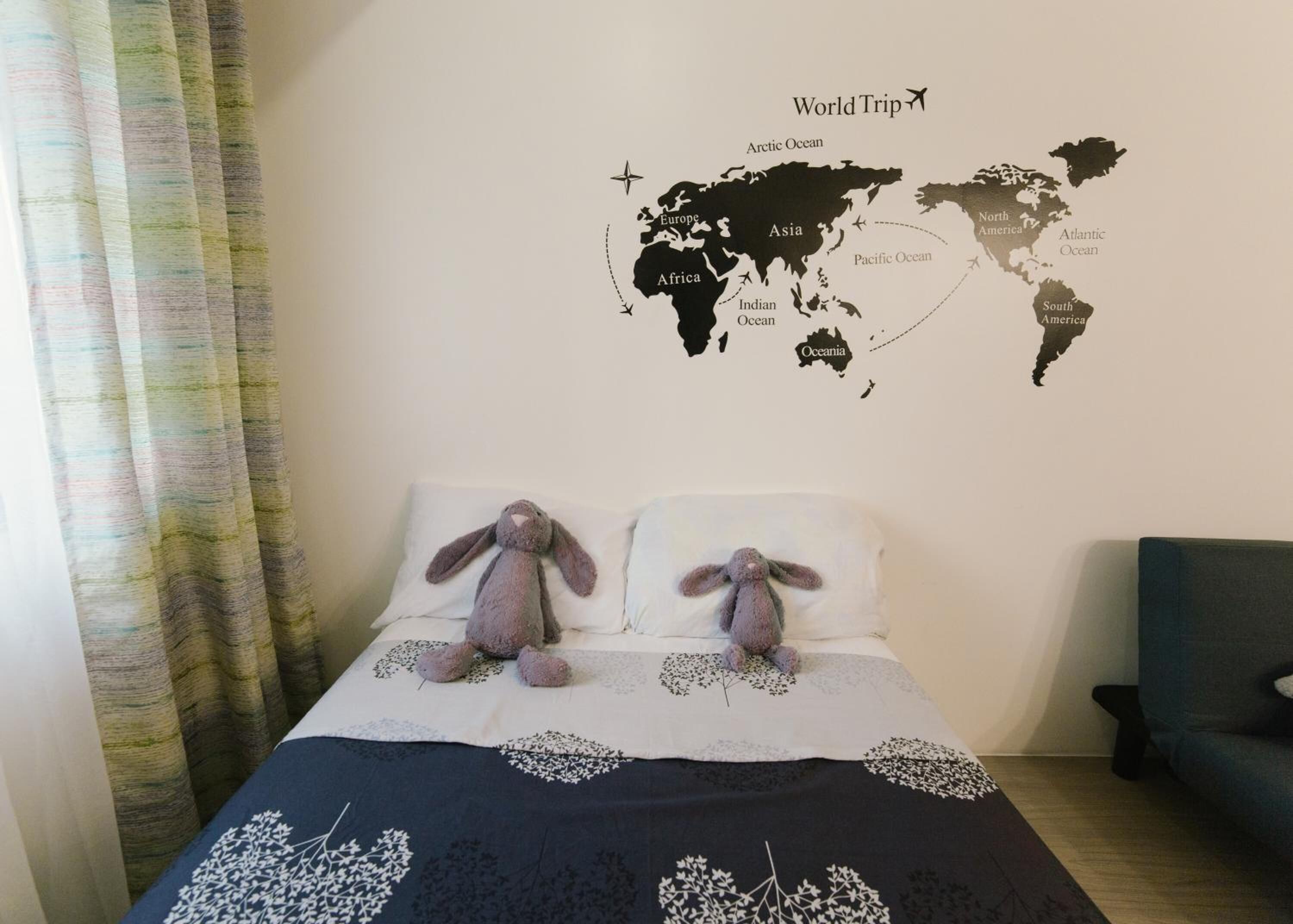 Un dormitorio con un mural de mapa del mundo, dos almohadas, una cama con colcha estampada floral y una ventana con cortinas.
