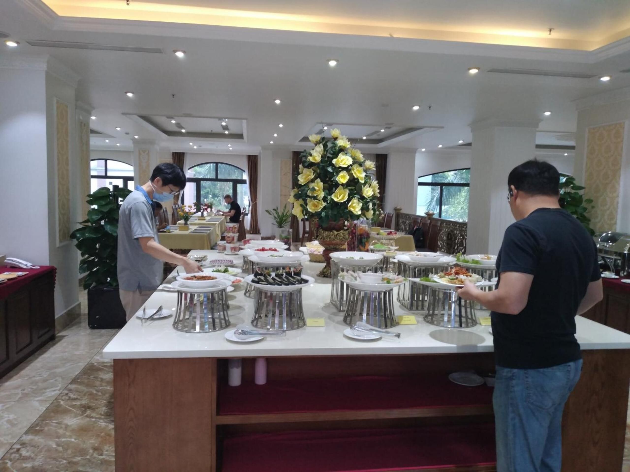 A buffet setup with multiple serving stations, a large floral centerpiece, and a well-lit room with a marble floor.