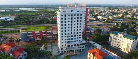 A high-rise hotel with a rooftop garden, a swimming pool, and a view of a river and cityscape.