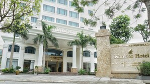 A large, white, multi-story building with a grand entrance, palm trees, and a sign for KimBao Hotel. - Kim Bao Hotel (Hai Phong)