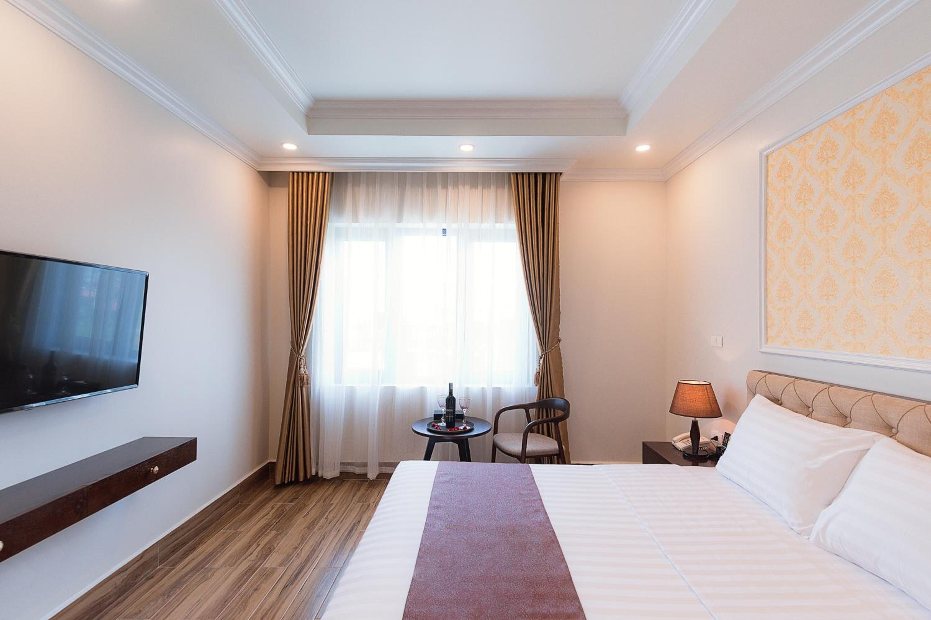 Een hotelkamer met een groot bed, een flatscreen-tv aan de muur, een klein tafeltje met een lamp en een stoel.