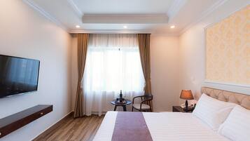 Een hotelkamer met een groot bed, een flatscreen-tv aan de muur, een klein tafeltje met een lamp en een stoel.