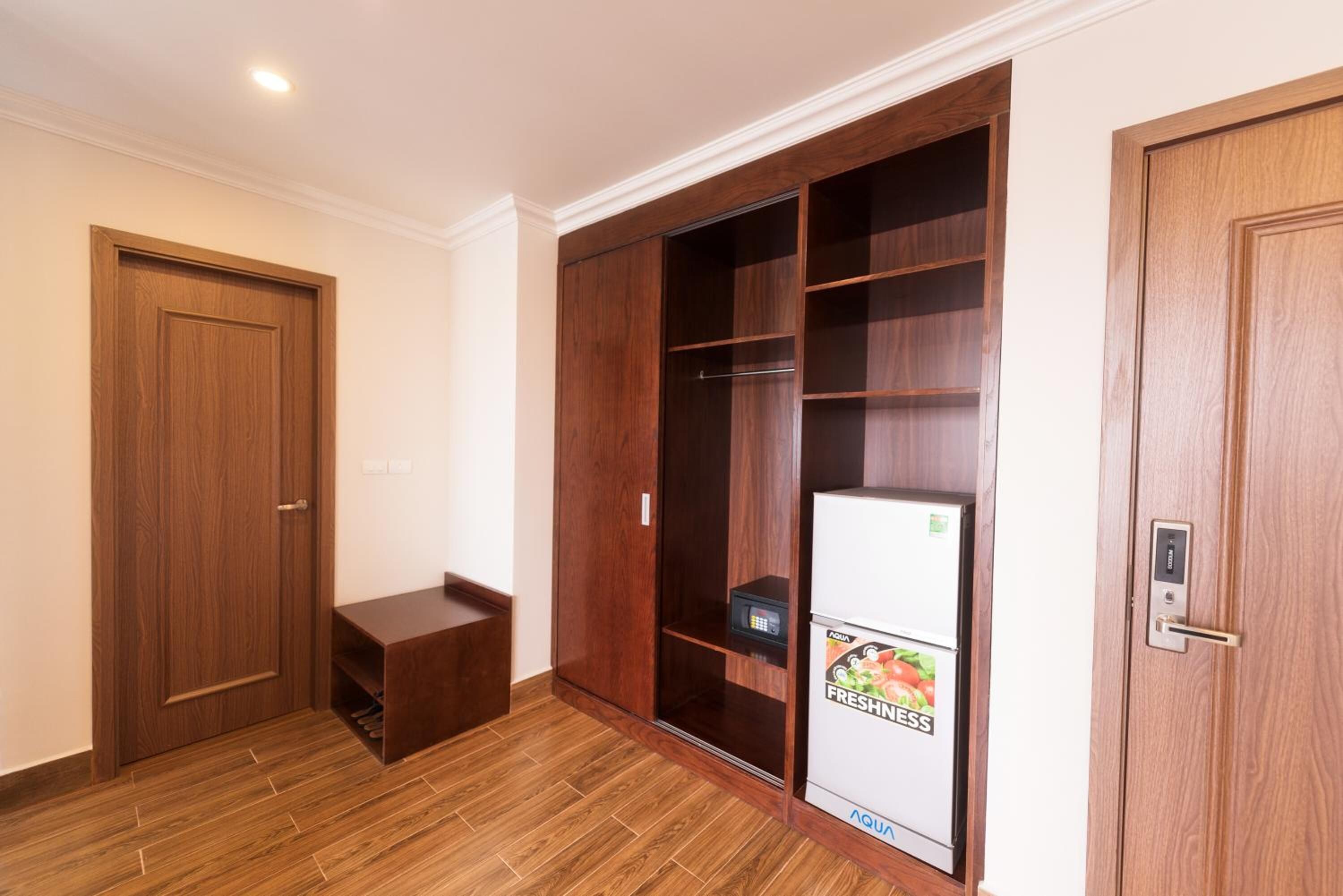 Una habitación con un armario de madera, un pequeño banco y un refrigerador con una etiqueta de productos frescos.