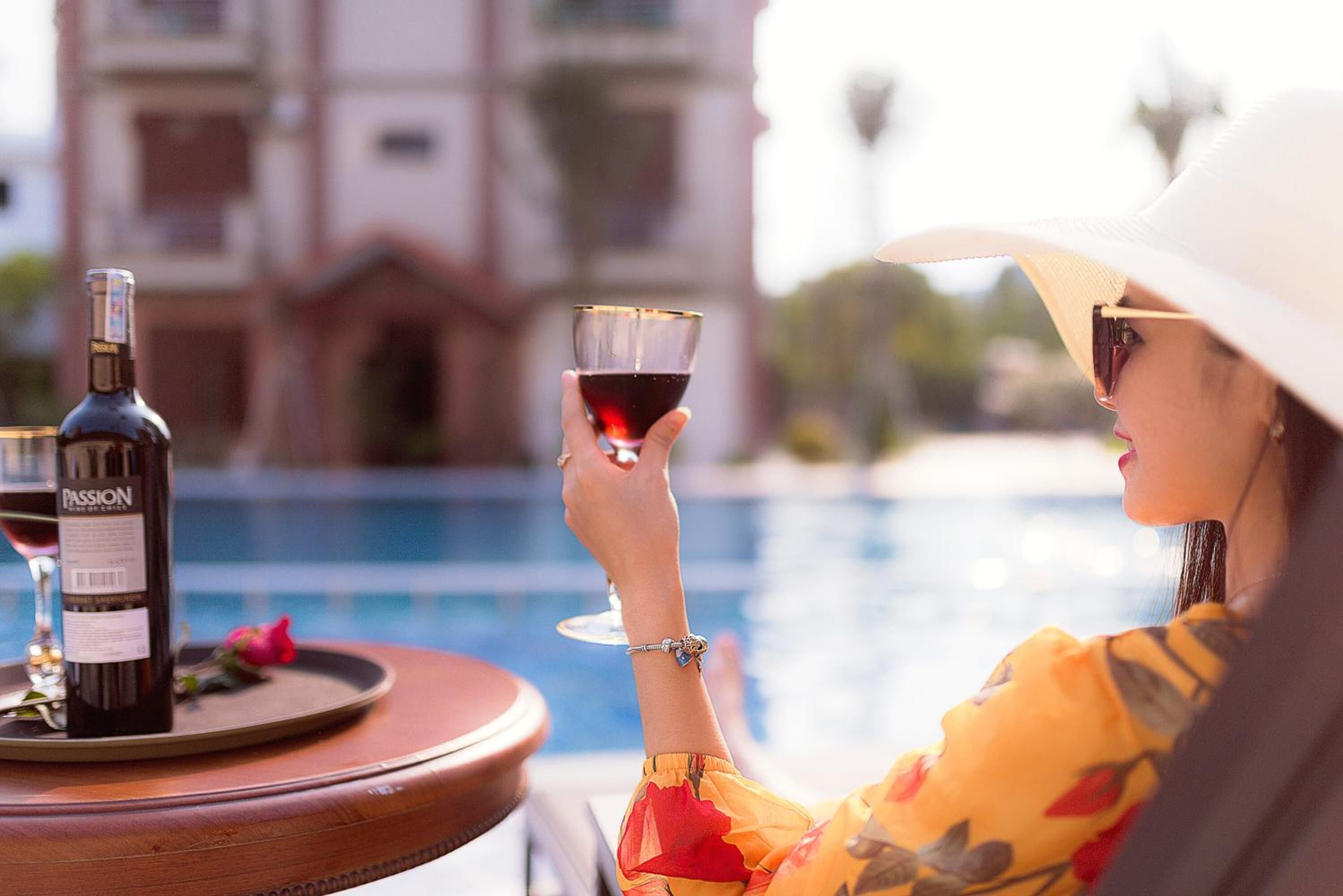 A person sitting by a pool with a bottle of wine and a glass.
