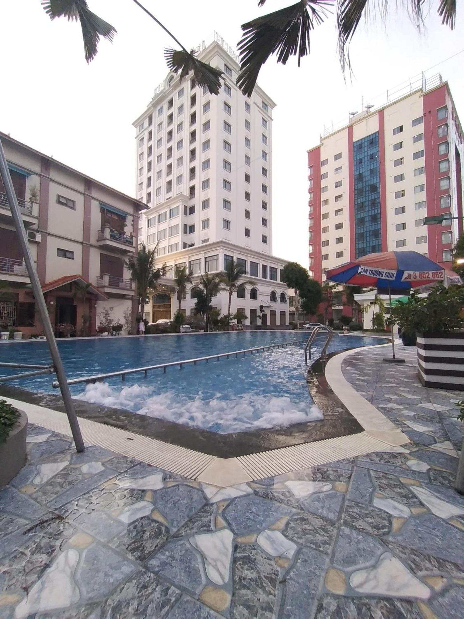 Una piscina con borde de piedra, rodeada de palmeras y edificios modernos.