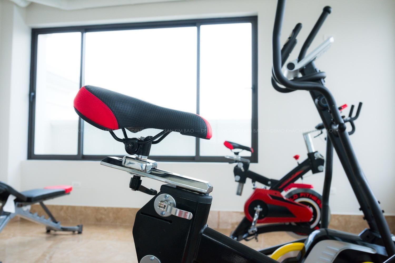 Un vélo d'appartement, avec une selle rouge et noire, un guidon et un mécanisme de pédalage.