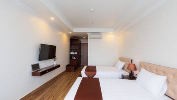A hotel room with two beds, a TV, a desk with a laptop, a lamp, and a wardrobe.