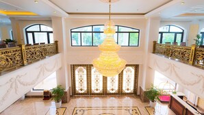 A grand lobby with a large chandelier, ornate railings, and a view of the outdoors through large windows. - Kim Bao Hotel (Hai Phong)