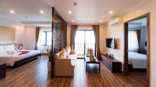 A hotel room with a bed, sofa, coffee table, TV, and a balcony with curtains. - Kim Bao Hotel (Hai Phong)