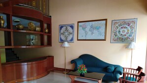 A living room with a blue sofa, wooden coffee table, and a wooden chair. There are two wall-mounted lamps and three framed pictures. A wooden cabinet with decorative items is on the left. - Sara Hotel (Labuan)