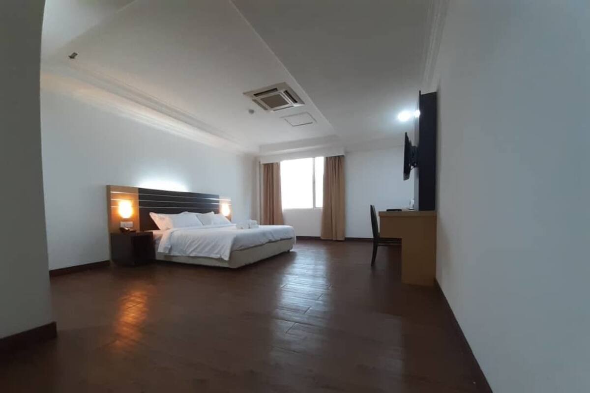 Amplia habitación de hotel con una cama grande, un escritorio, una silla y un televisor en la pared.