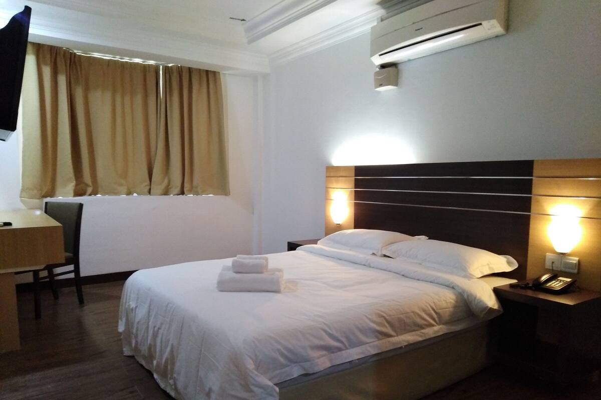 Una habitación de hotel con cama, mesita de noche, lámpara y aire acondicionado.