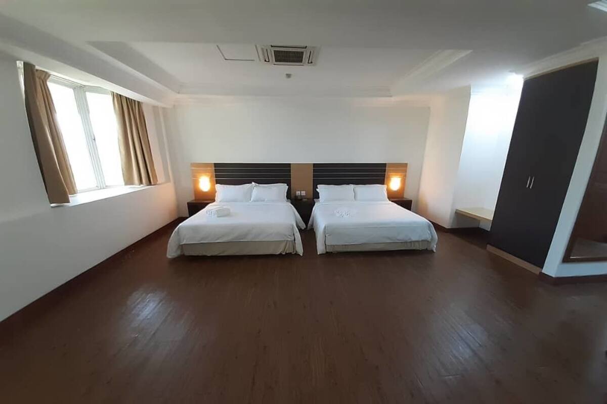 Una habitación de hotel con dos camas, un ventanal con cortinas, un armario y una rejilla en el techo.