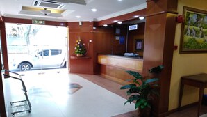 A reception area with a reception desk, a potted plant, and a painting on the wall. - Sara Hotel (Labuan)