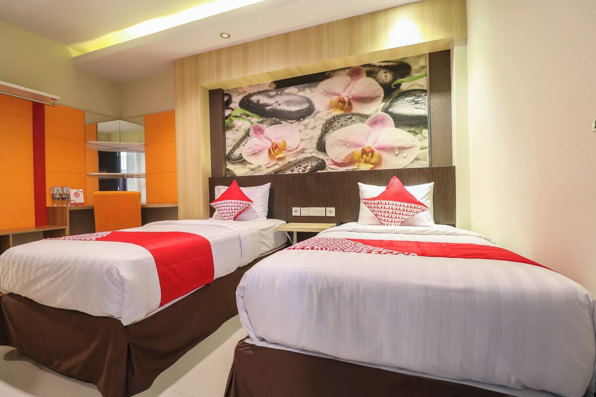 A hotel room with two beds, each with white bedding and red accents, a large mirror, and a wall-mounted artwork of orchids.