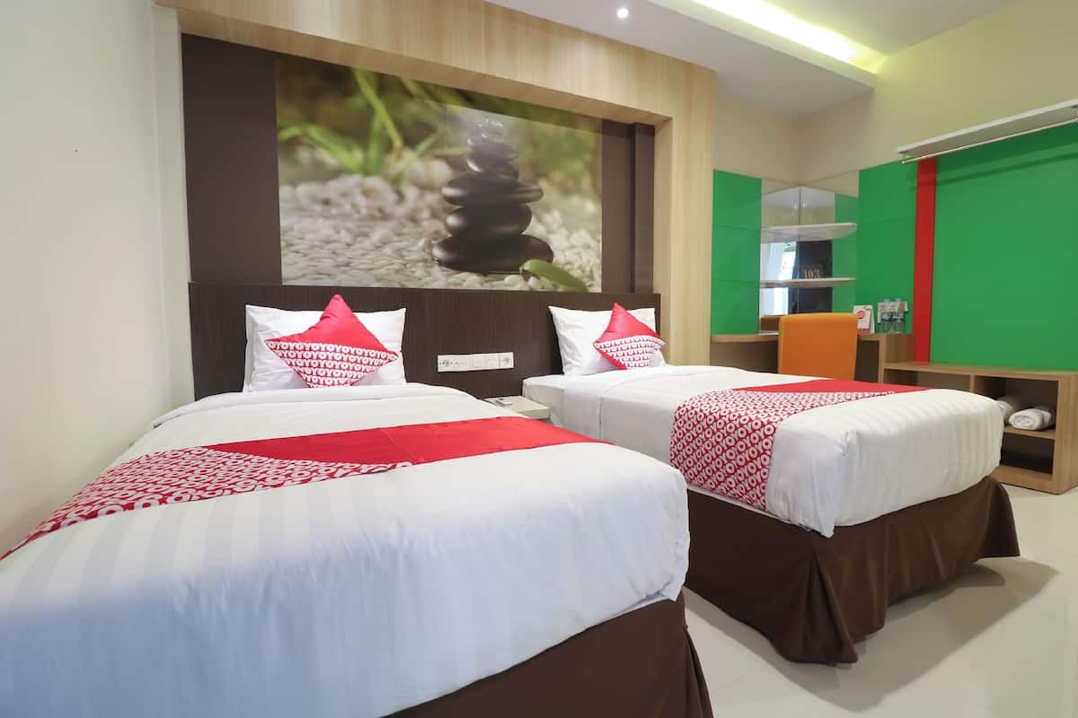 A hotel room with two beds, each with white bedding and red accents, a large wall-mounted TV, and a green accent wall.