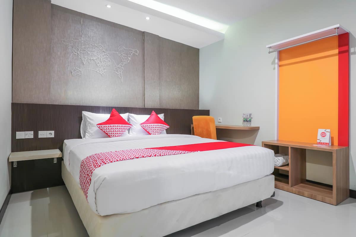 A modern hotel room with a large bed, a wooden nightstand, a small table with a bottle, and a red and white decor theme.