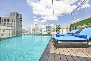 Una piscina en la azotea con sillones de descanso y vistas al horizonte de la ciudad.