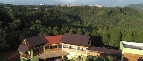 Un edificio grande de varios pisos con techo rojo, rodeado de abundante vegetación y montañas al fondo.