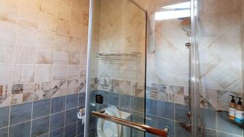A bathroom with a glass-enclosed shower, a toilet, and a sink.