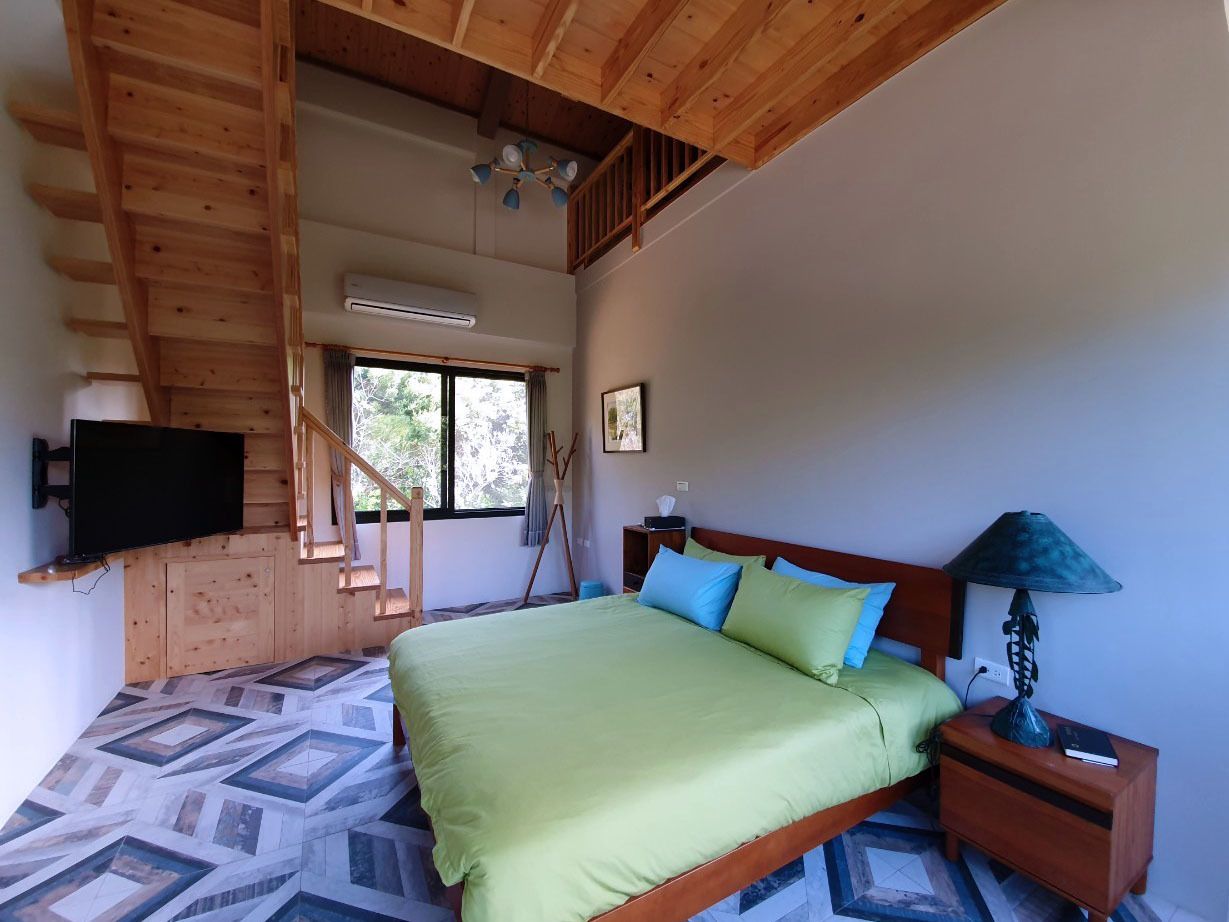 A bedroom with a bed, a nightstand, a lamp, a TV, and a staircase.