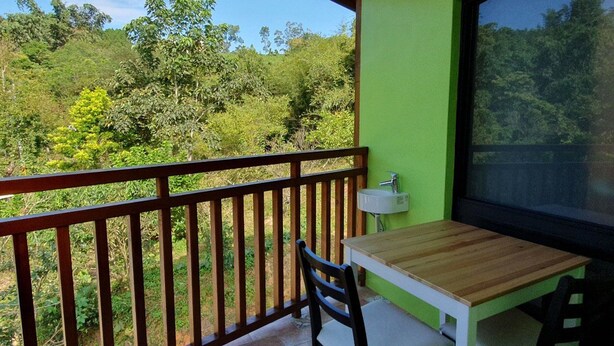 Ein Balkon mit Holztisch und -stühlen, einem Spülbecken und Blick auf einen üppigen, grünen Wald.