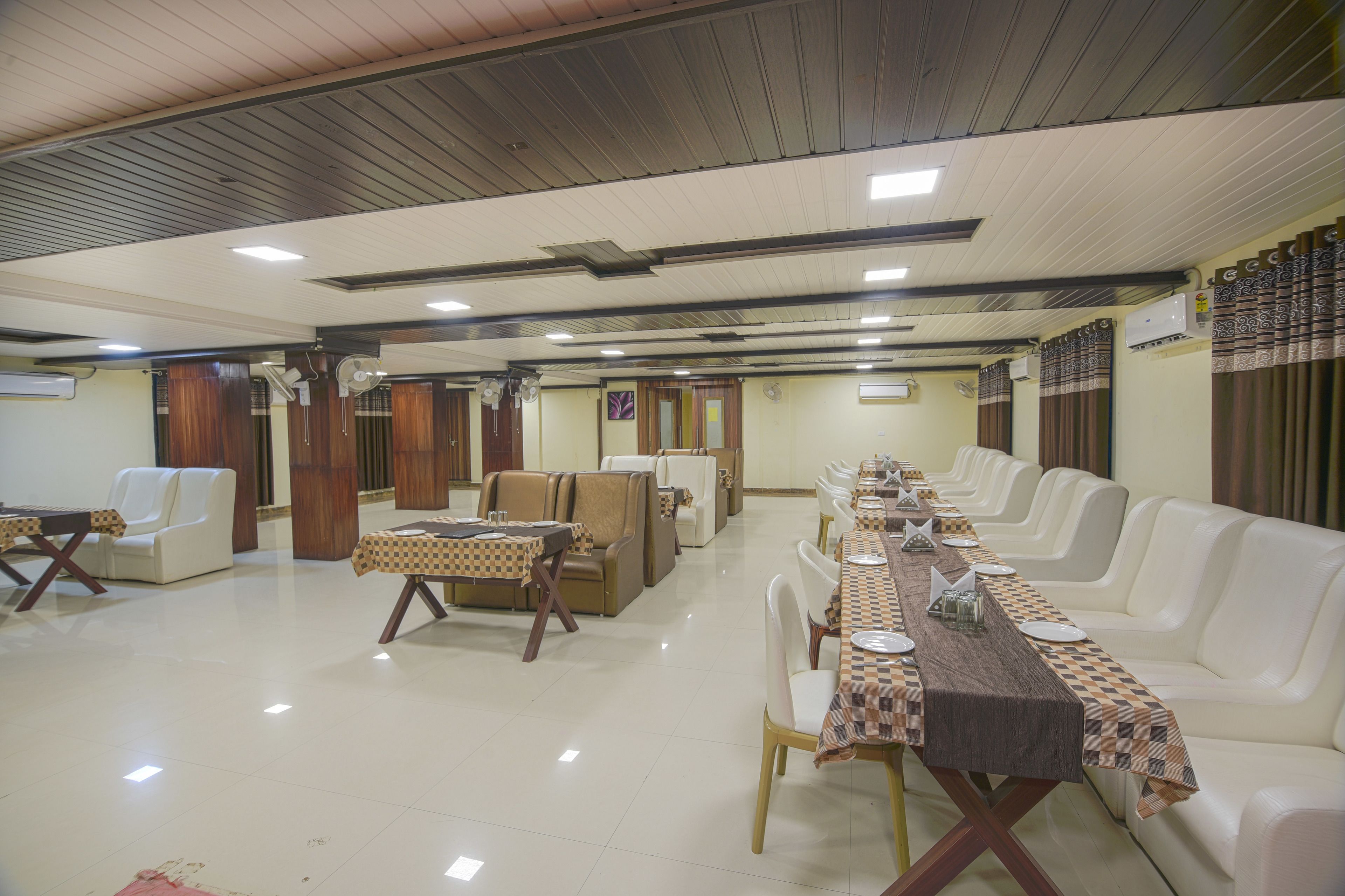 A spacious dining area with a long table set for a meal, surrounded by white leather sofas and chairs.